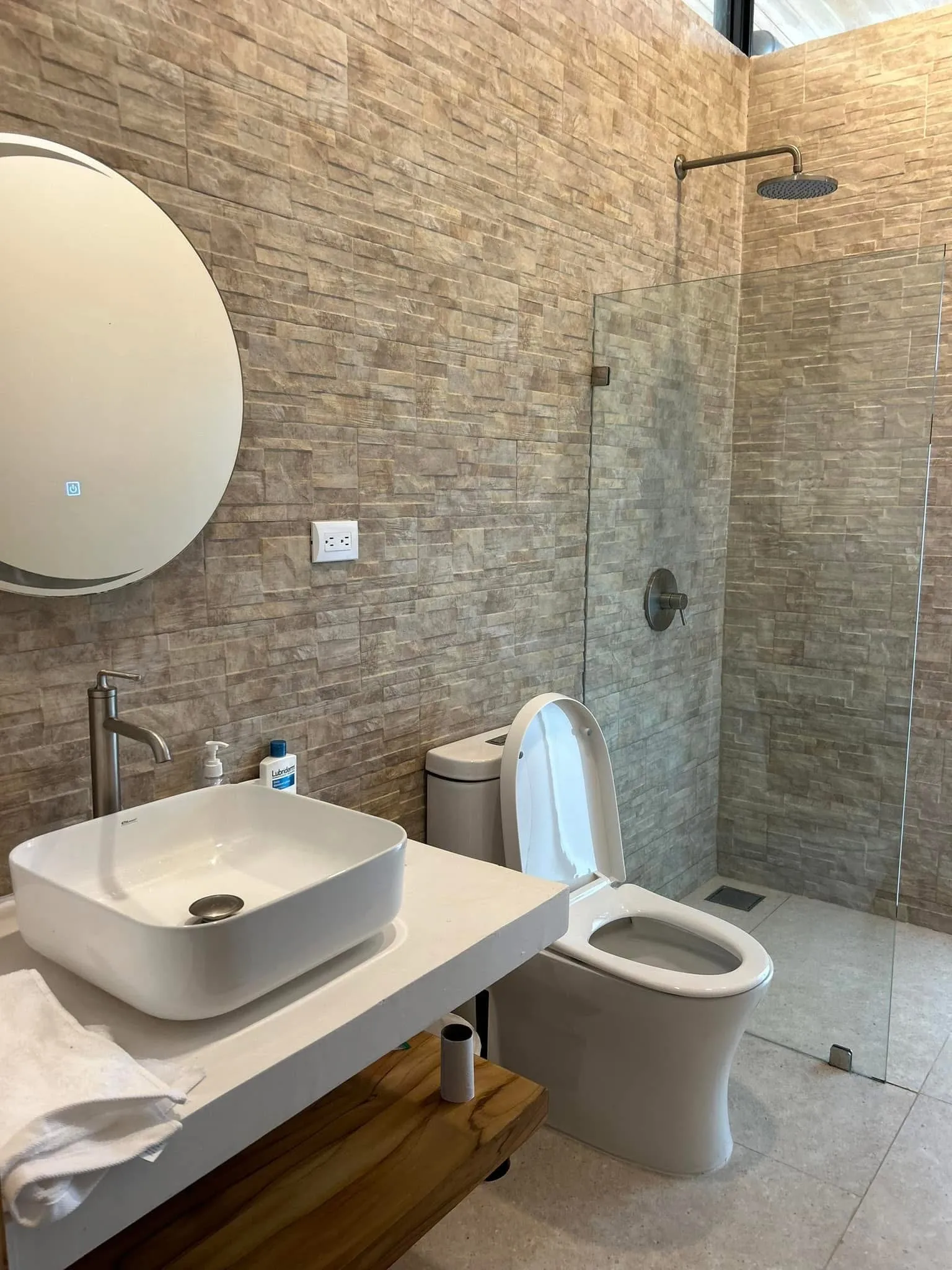Casa Delicias bathroom clad in natural stone tile with a vessel sink, open shower, and teak-slat ceiling.
